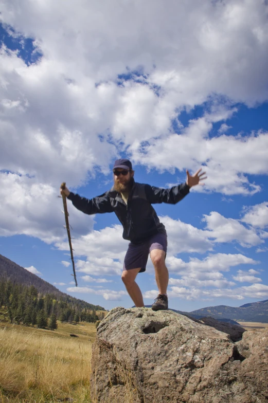 man standing on top of a large rock holding a stick