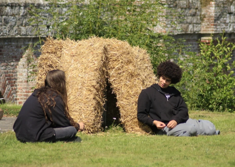 two people are sitting on the grass and looking at cell phones