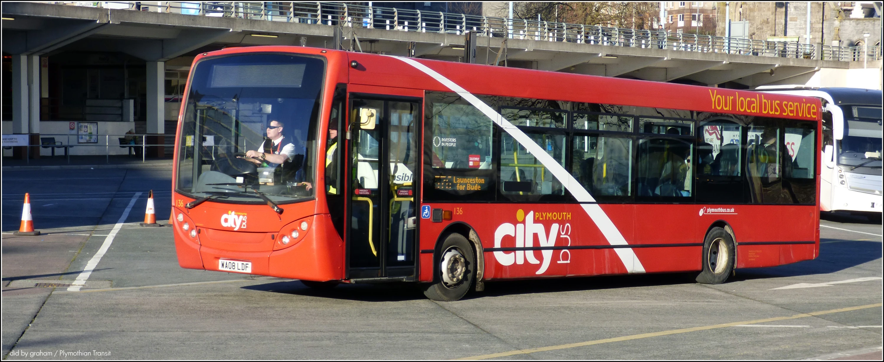 an orange red and white bus driving through a parking lot