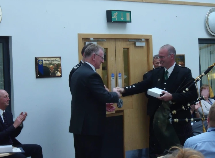 two men in suits are standing at a door and a table in the background