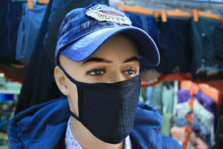 a hat with a black face mask, and a blue cap on a mannequin's head