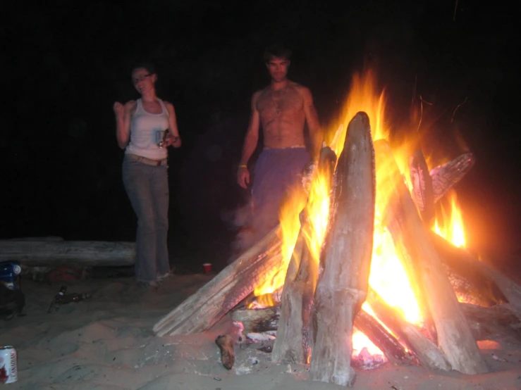 two people standing around a fire at night