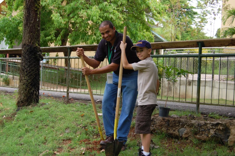 a man and a child are holding onto tree stems with a metal fence in the background