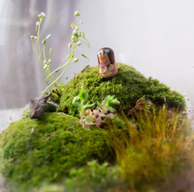 a miniature figure is sitting on a mossy patch