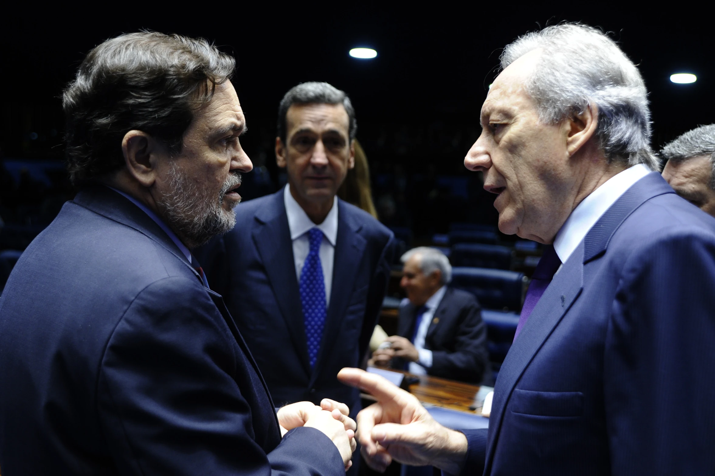 two men in suits standing in front of a man in suit and tie