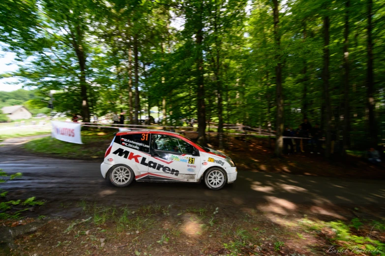 a small rally car taking a jump on a road in the woods