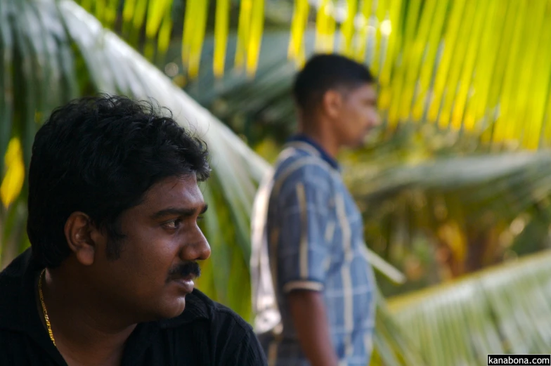 a man looking at another mans shoulder with green trees in the background