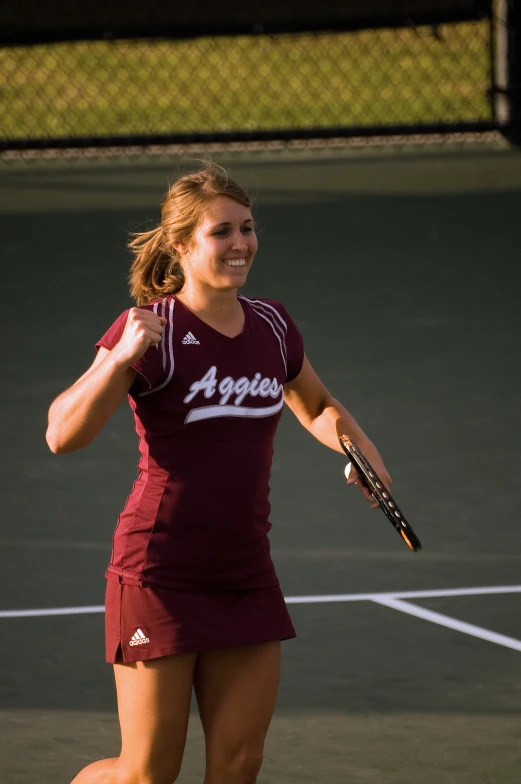 woman in maroon top and shorts holding up her tennis racket