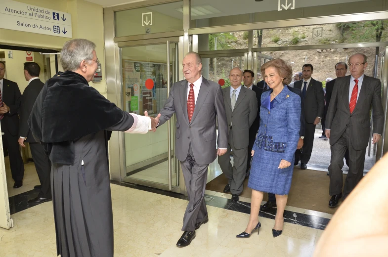 two business men shake hands while an other people watch