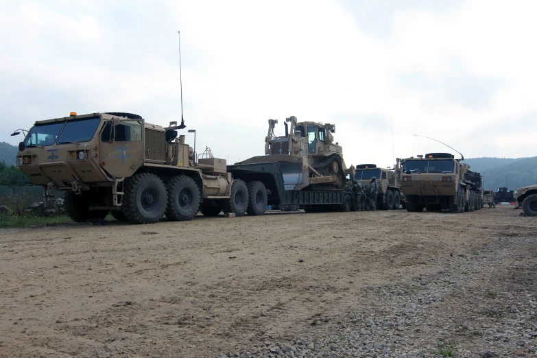 there are military trucks and tow trucks driving in the dirt