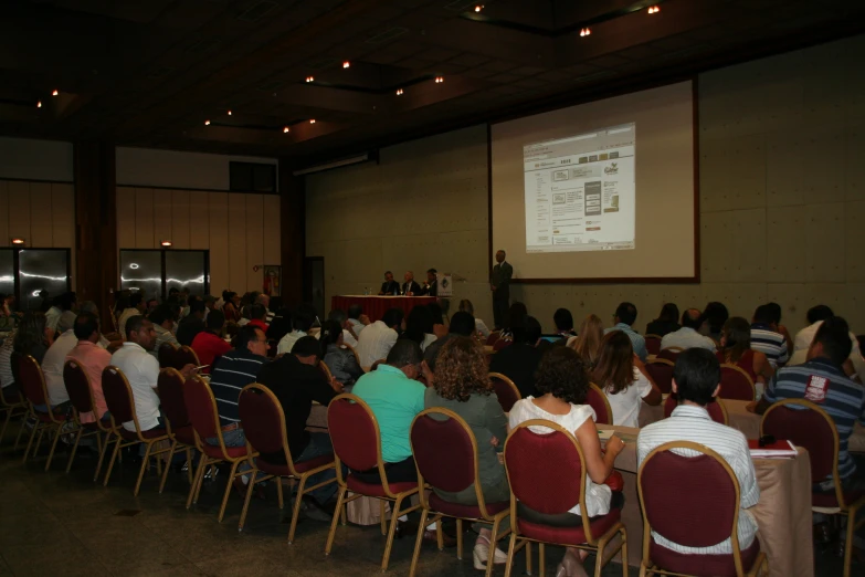 a group of people in a room with chairs watching a presentation on the screen