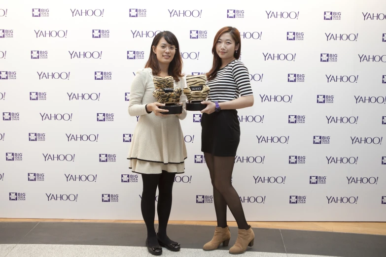 two women holding trophies on a stage next to a wall