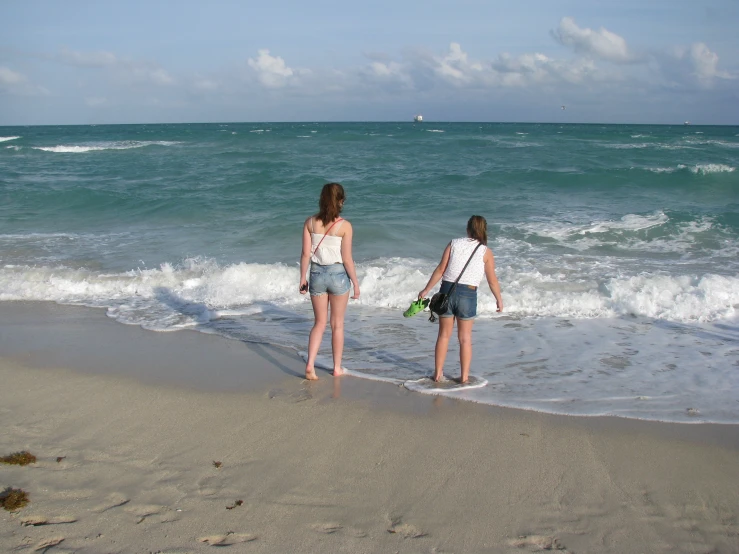 two young women standing at the edge of a beach