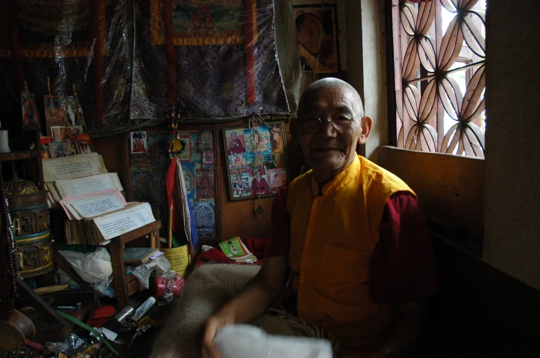 an older man sits in the corner with lots of other things behind him