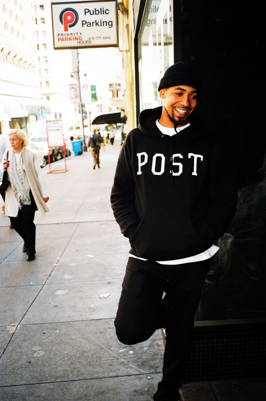 a man in a black sweatshirt standing by the side of a building