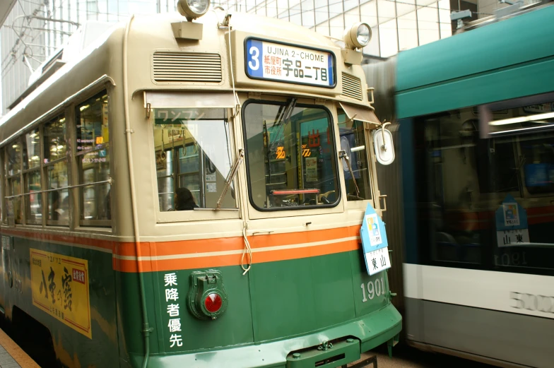 an old asian trolley with an orange stripe on its side and green and white stripes on it, near a large building