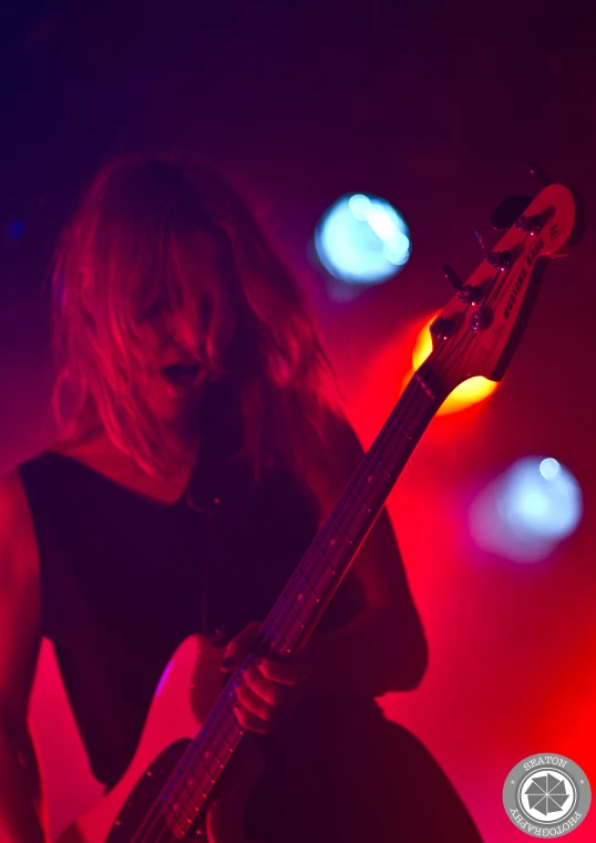 a woman in black is playing guitar in a purple light