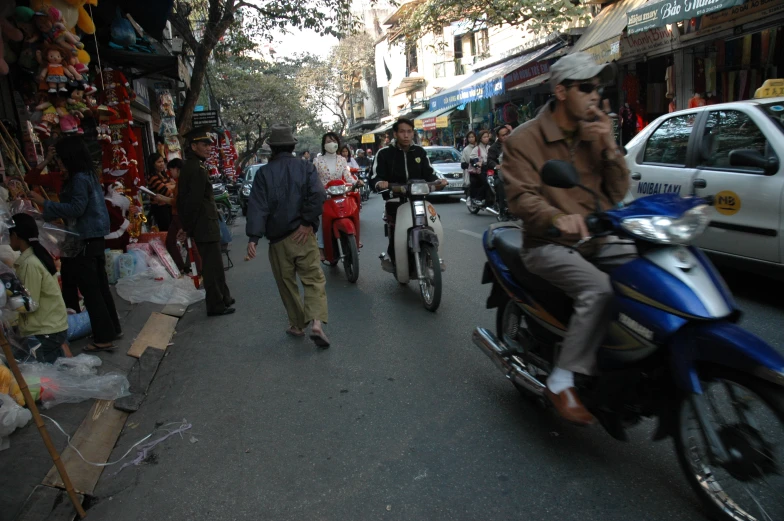 people walking down a street with cars, motorcycles, and shops