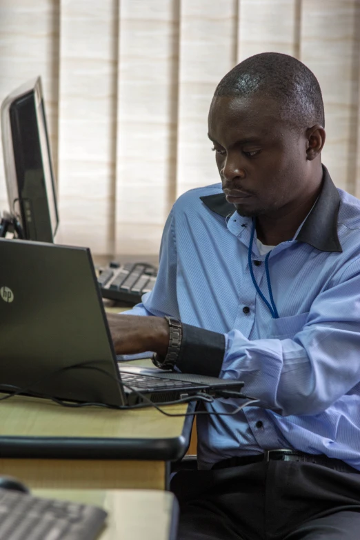 a man works on his laptop computer while wearing a blue shirt