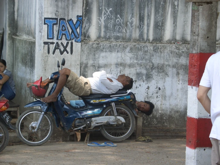 a man lying on a motorcycle in the shade