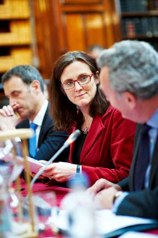 three people sitting at a table while one holds a microphone and points