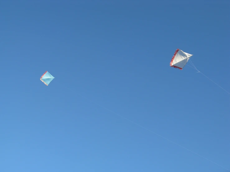 two kites fly high in the sky next to each other