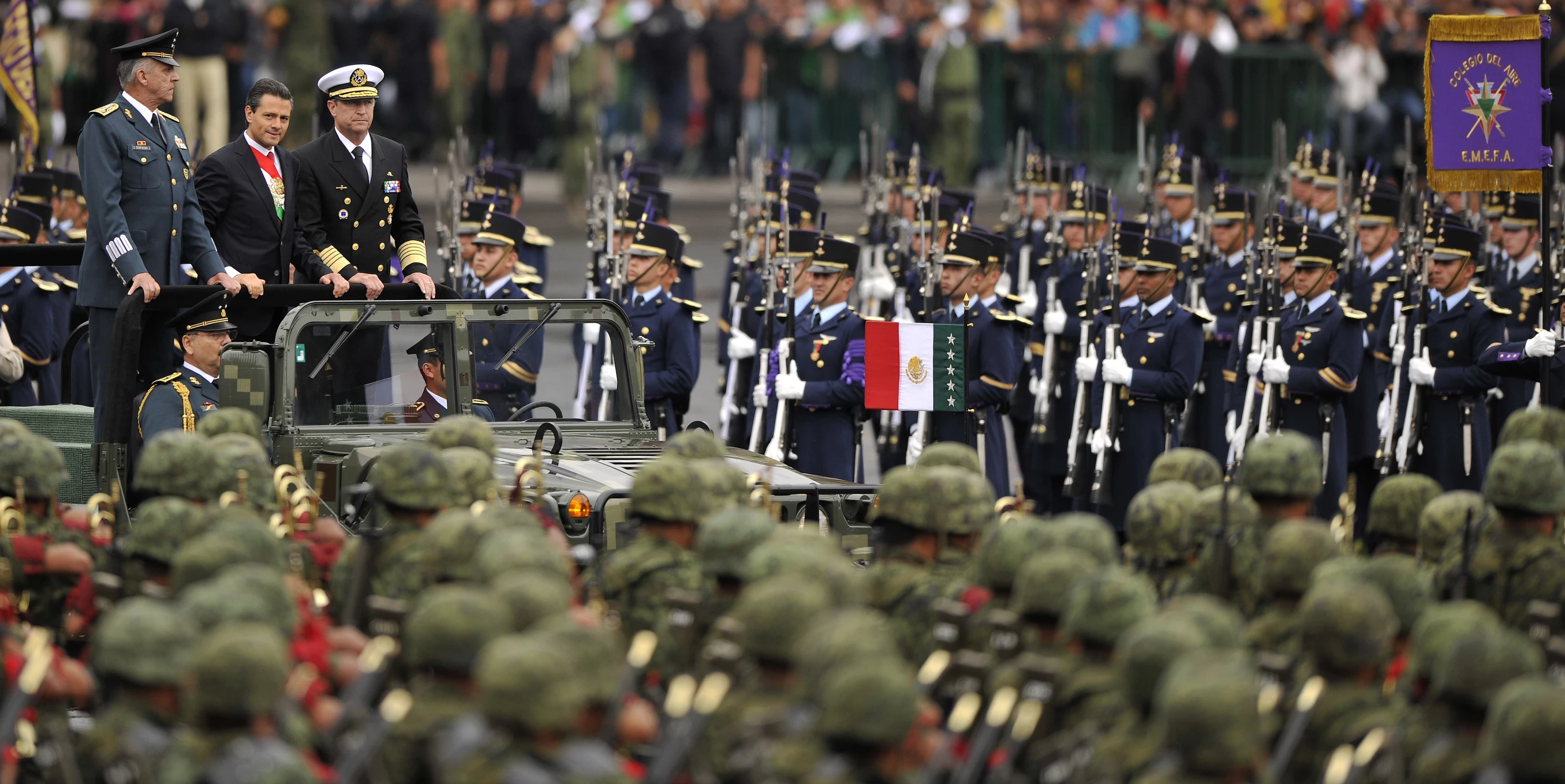 military officers walking in formation as they pass by a group of men on a jeep