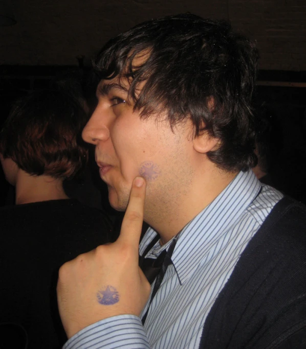 a man in a striped shirt with tattoos is holding up his hand to his ear