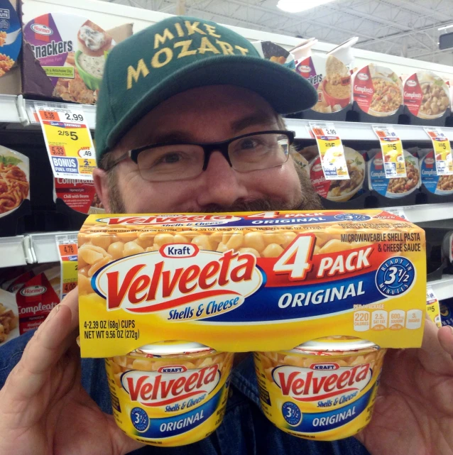 a man holding up four cups of velveeta in a supermarket