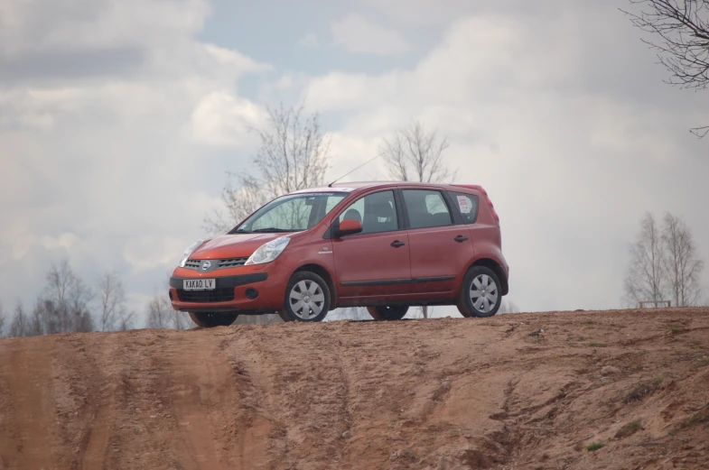 the small car is parked on the dirty road