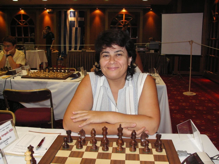 a woman is sitting at the table and looking into the camera behind a chess board