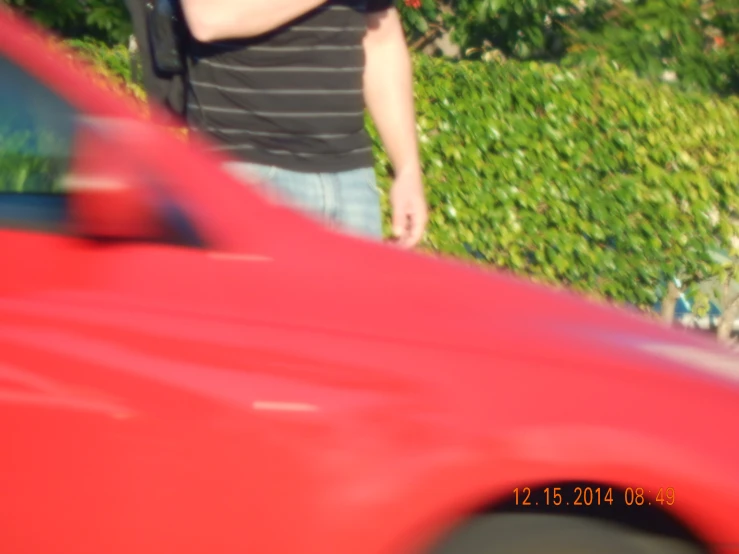 a person standing near a red car and holding an object in his hand
