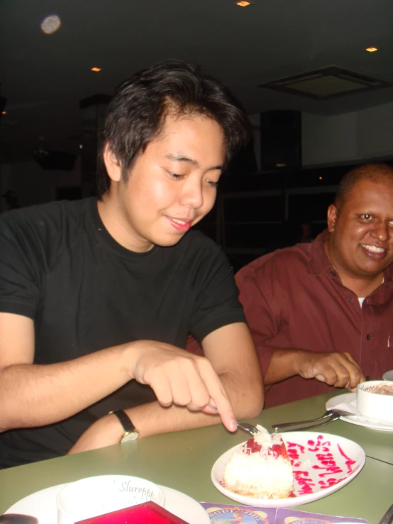 two men sitting at a table  up cake