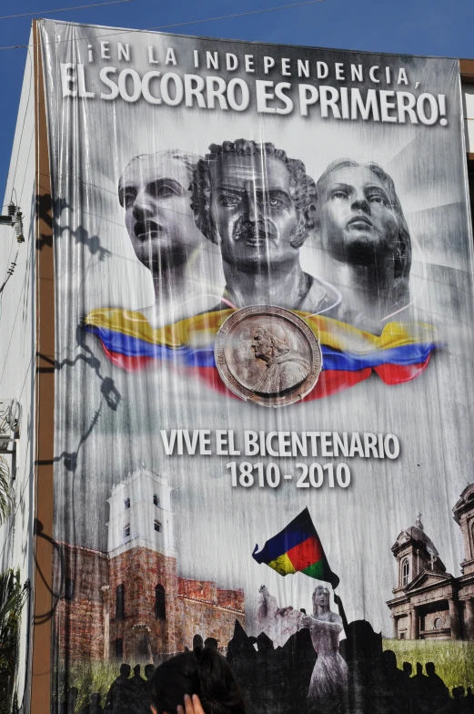 a poster in the form of a man's face and two men with their hands on his back against a blue sky