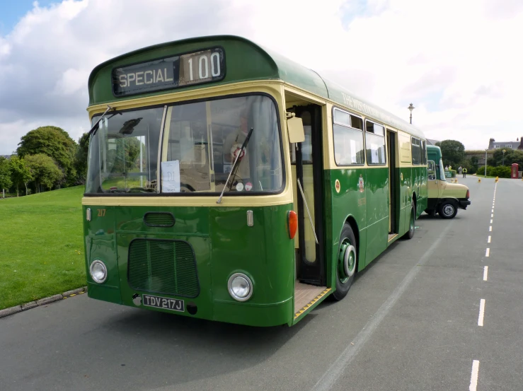 two green buses parked on side of road next to grass