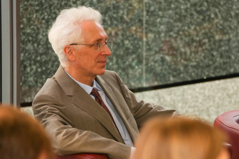 a man in glasses and a suit sitting in front of a group