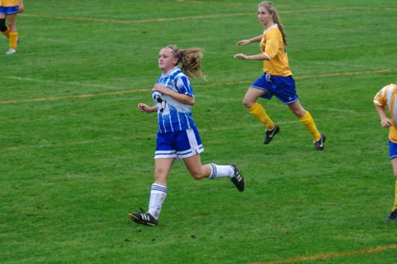 three girls running after a soccer ball on a field