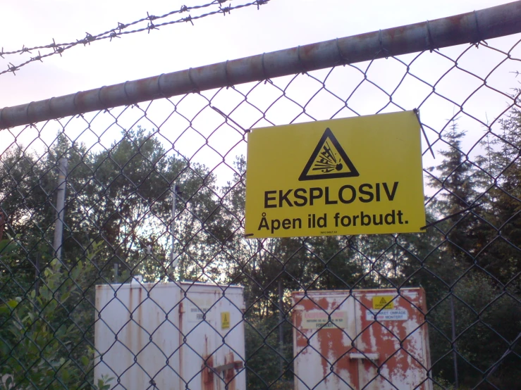 a yellow and black sign on chain link fence