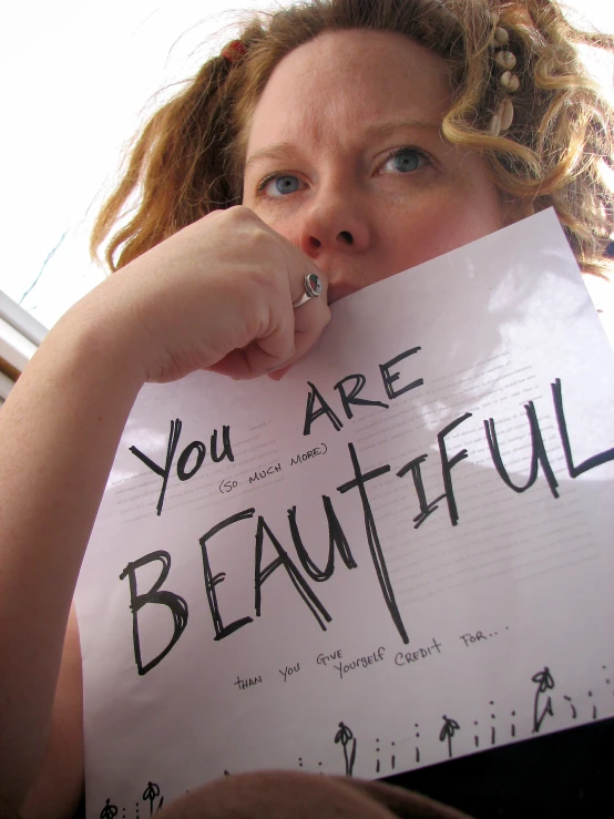 a woman is holding up a sign saying you are beautiful