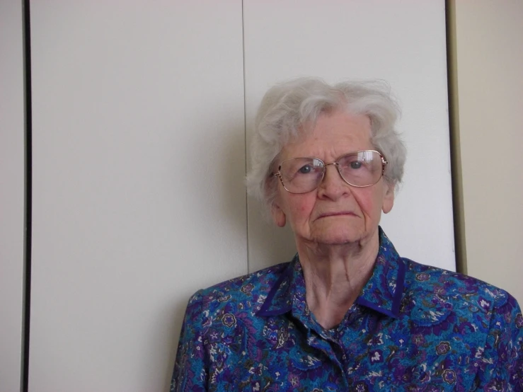 an old woman wearing glasses and a blue shirt with a bird on it