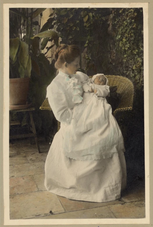 a woman in white dress holding a baby next to plants
