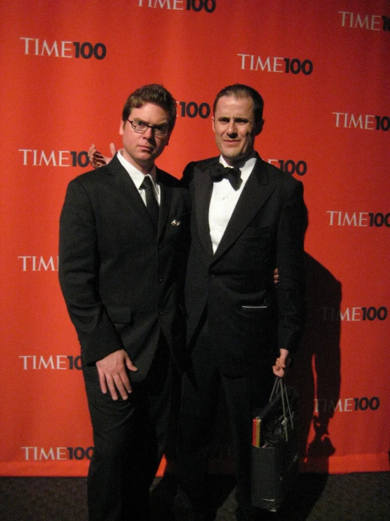 two men in suits and ties stand in front of a time 100 sign