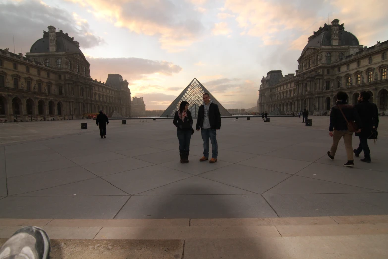 several people are walking in a courtyard near a pyramid