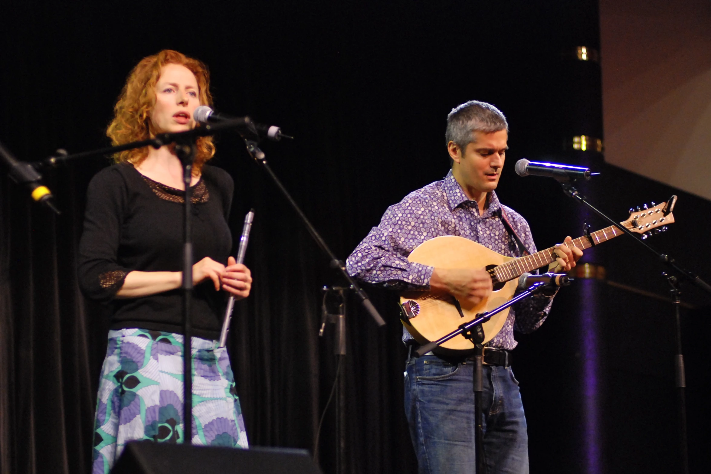 man playing guitar while woman sings into microphones