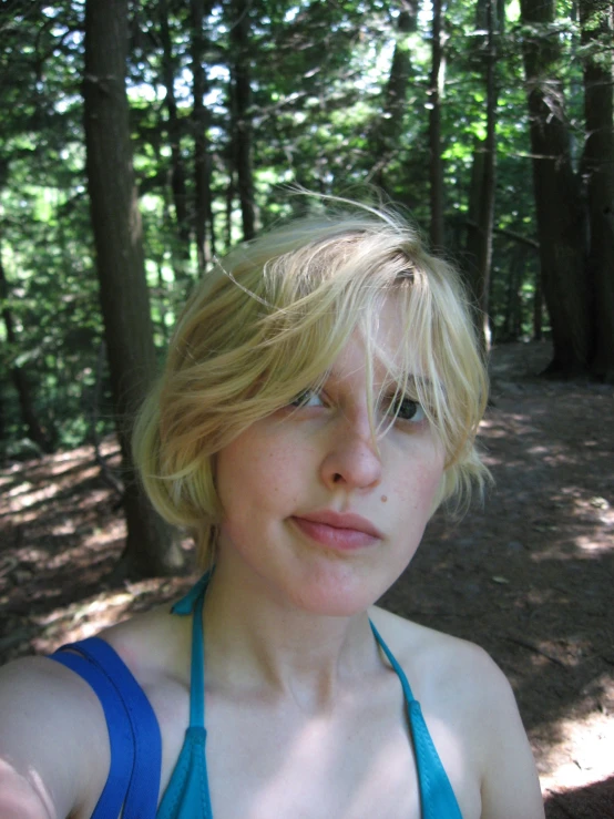 a young woman stands in a forest wearing a blue bikini top