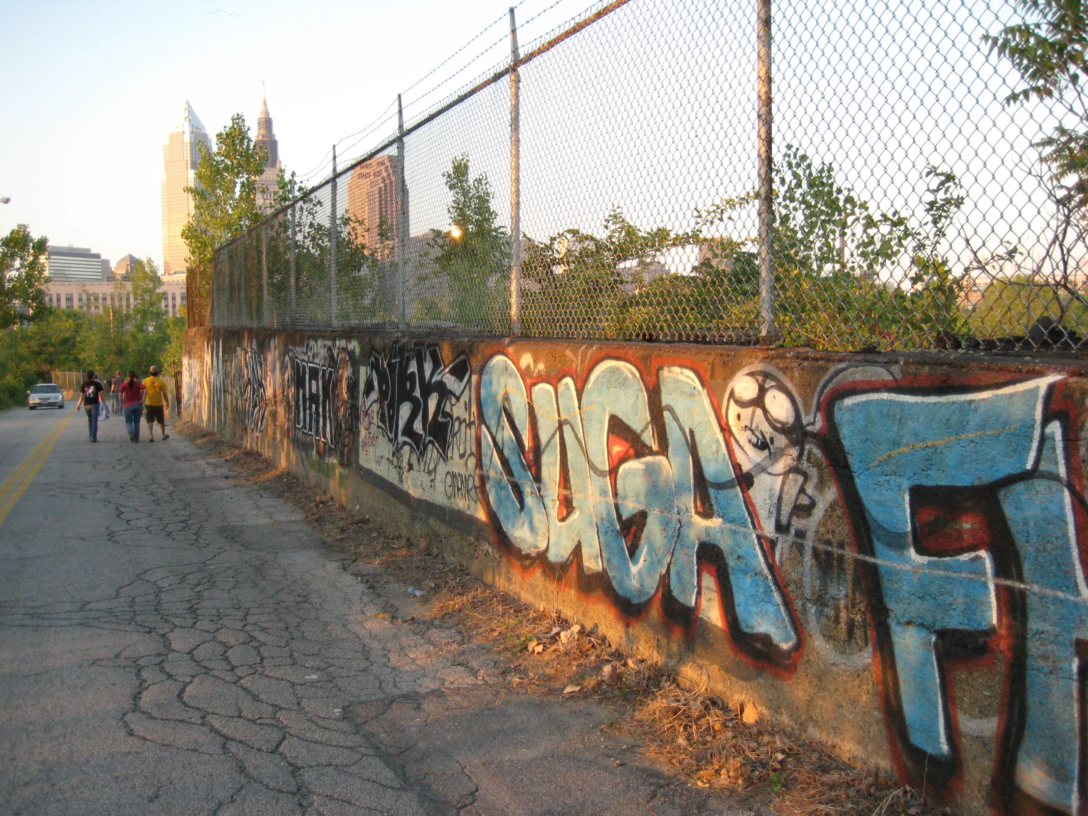 a fence has been decorated with graffiti and some people are walking in the distance