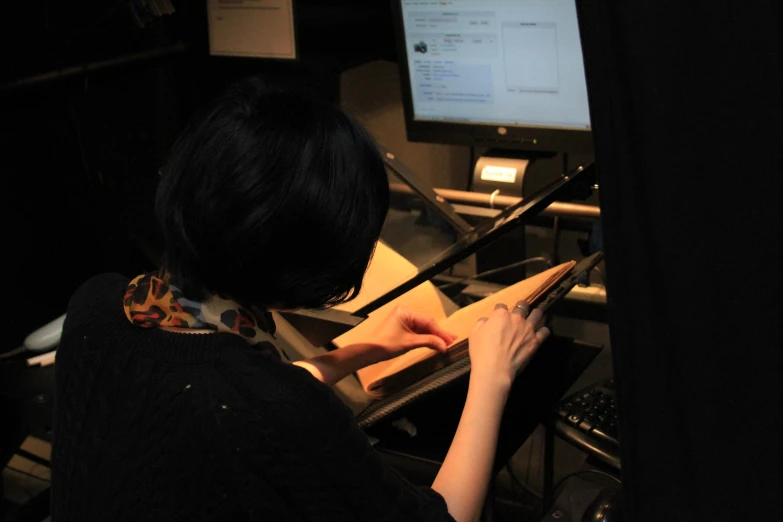 a woman sitting next to a computer desk writing on a piece of paper