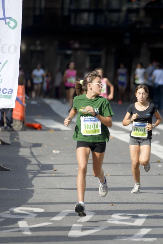 two girls race together down the road in front of a crowd