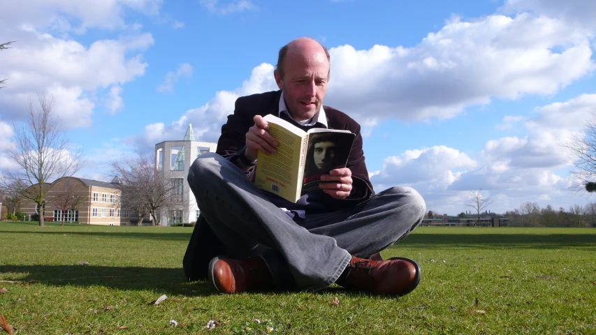 an old man sitting on the grass reading a book