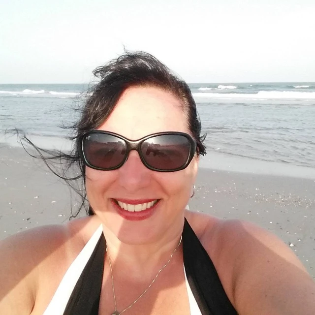 a woman in glasses standing on a beach